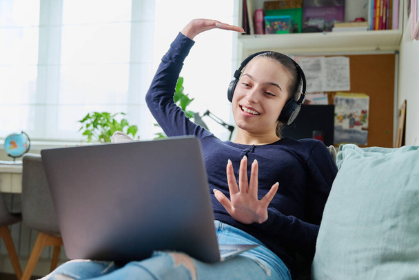 Teenage girl in headphones having fun looking at a laptop, music video for leisure time relaxation, sitting on the couch at home - Photo, image