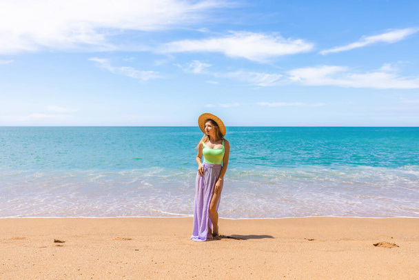 Attractive woman in swimwear on the beach or ocean, relaxes on vacation, calm and serenity of the exotic location. Smiling girl in a straw hat enjoying sunshine and leisurely of tropical getaway - Photo, image