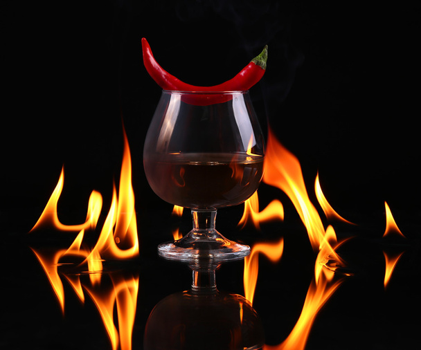 Hot chili pepper in a  cognac ballon with a fire on a black background - Foto, Imagem