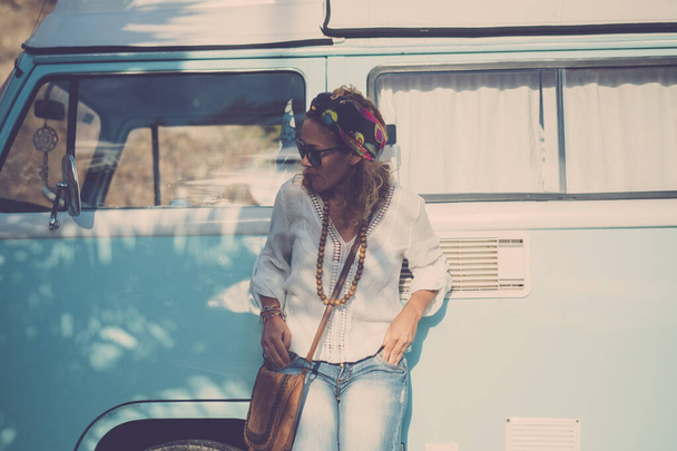 vrouw tegen blauw klassiek busje reizen en genieten van hippe levensstijl vrije tijd outdoor activiteit alleen. Concept van voertuig vakantie en het leven. Casual trendy vrouwelijke mensen. Retro stijl kleding en camper - Foto, afbeelding