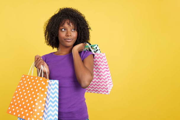Fajna kobieta z afro włosów i toreb na zakupy w studio z żółtym tle - Zdjęcie, obraz