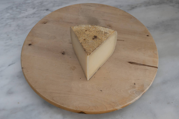 French culinary Still Life. Piece of cheese Ossau Iraty placed on a wooden pan - Photo, Image