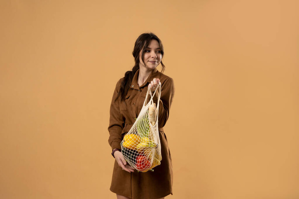 Zero waste concept. Young beautifull brunette woman holding reusable mesh shopping bags with vegetables, products. Eco friendly mesh shopper. Zero waste, plastic free concept - 写真・画像