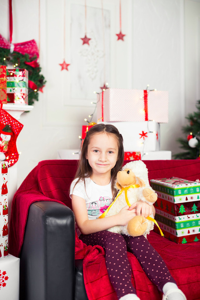 Little girl sitting on coach holding stuffed toy, Christmas gift, tray in the background - Фото, зображення