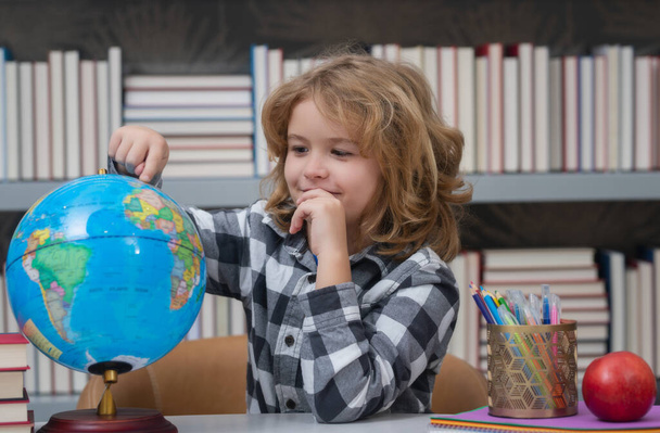 School kid pupil looking at globe in library at the elementary school. World globe. School kid 7-8 years old with book go back to school. Little student. Education concept - Foto, imagen