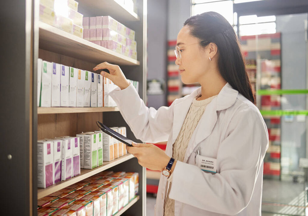 Pharmacy, inventory and Asian woman with tablet, checklist and healthcare medicine. Japanese female pharmacist, lady and medical professional with device, pills and update product information. - Zdjęcie, obraz