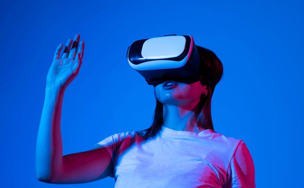 Brunette woman in virtual reality headset playing a video games with a friends and gesturing with a hands. Future gaming concept - Foto, imagen