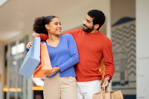 Family Weekend In Shopping Center. Happy Husband And Wife Posing With Paper Shopper Bags Having Fun During Sales Season Outdoor. Couple Buying New Clothes Together. Discount Offer Concept - Photo, Image