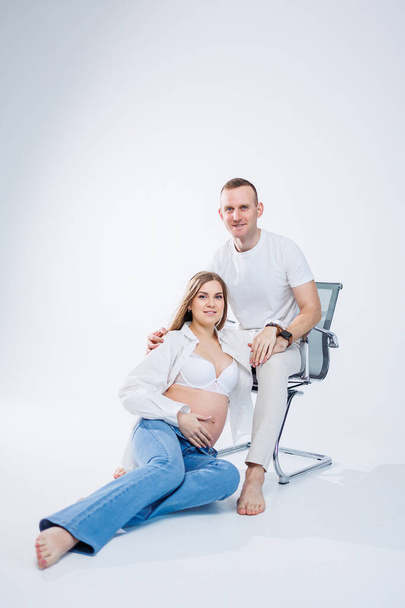 A pregnant woman and a man are standing on a white background. Beautiful young attractive pregnant woman. Family, marriage, childbirth concept. Happy pregnant couple - Photo, image