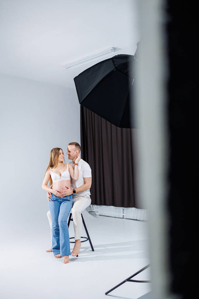 Happy young couple expecting a baby in white t-shirts and jeans on a white background. happiness of pregnancy and childbirth. A happy married couple is expecting a child - Foto, imagen
