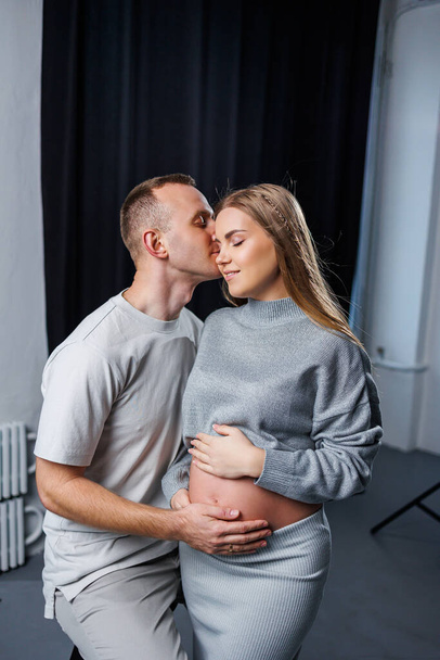 Happy and attractive pregnant woman and her husband are hugging and happy in anticipation of childbirth. Cheerful family pregnant couple - Fotó, kép