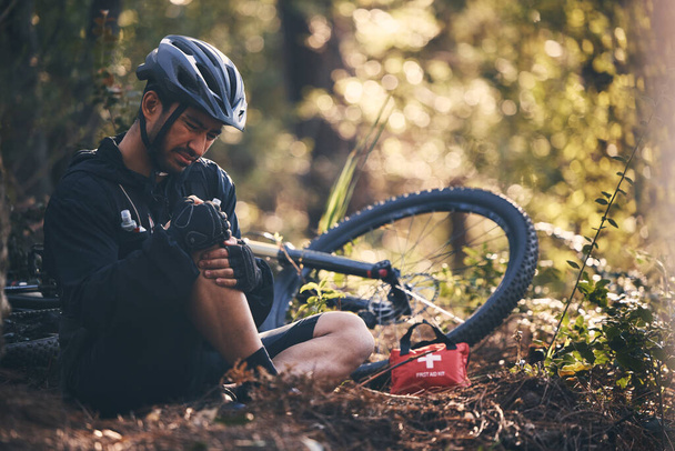 Sports man, injury and first aid outdoor while cycling on mountain bike in nature with leg or knee pain. Athlete person on ground in forest for fitness exercise, training or workout accident or fall. - Photo, Image