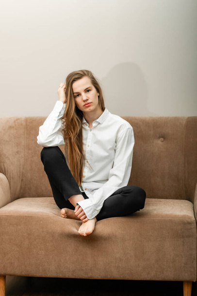 красивая молодая женщина с длинными волосами сидит на бежевом диване - Фото, изображение