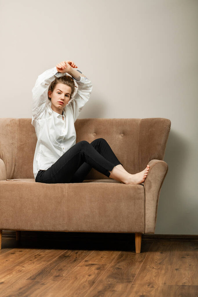 beautiful young woman with long hair sitting on a beige sofa - Foto, afbeelding