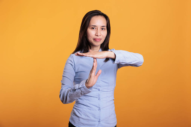 Filipínská žena ukazuje timeout a break gesto ve studiu, dělá t tvar znamení s rukama pozastavit akci. Vážná mladá dospělá osoba, která odmítá stát nad žlutým pozadím. Zastavit koncept - Fotografie, Obrázek