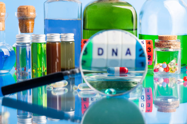 DNA pill on the background of a laboratory table with medicines and preparations. View through a magnifying glass. - Photo, image