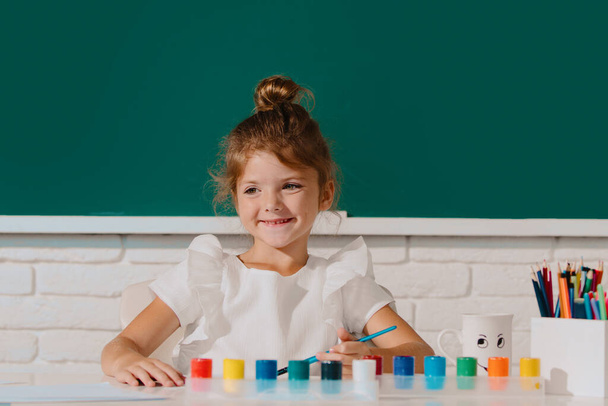 Boya rengi ve fırçayla resim yapan şirin bir kız çocuğu. Okulda resim çizen tatlı bir kız. - Fotoğraf, Görsel