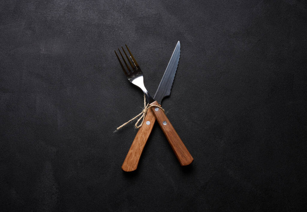 Fork and knife with wooden handle on black background, top view - Zdjęcie, obraz
