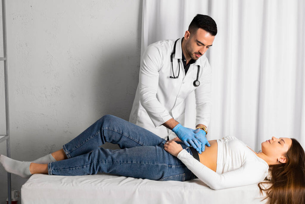 Lekarz w czystych lub sterylnych rękawicach wykonuje badanie lekarskie pacjentki naciskając na jej brzuch.. - Zdjęcie, obraz
