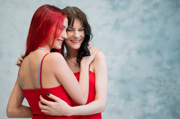 A close-up portrait of two tenderly embracing women dressed in identical red dresses. Lesbian intimacy - Zdjęcie, obraz
