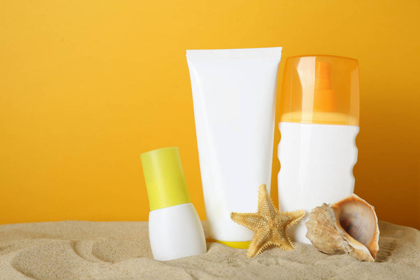 Different suntan products, seashell and starfish on sand against yellow background. Space for text - Фото, изображение