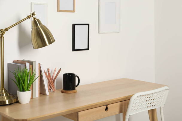 Comfortable workplace with wooden desk near white wall indoors - 写真・画像
