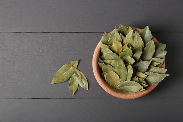 Aromatic bay leaves in wooden bowl on gray table, flat lay - Photo, Image