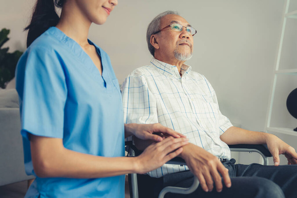 Νοσοκόμα και ένας ικανοποιημένος ηλικιωμένος σε αναπηρική καρέκλα στο σπίτι, σε οίκο ευγηρίας. Ιατρική περίθαλψη για ηλικιωμένους ασθενείς, κατ 'οίκον περίθαλψη για συνταξιούχους. - Φωτογραφία, εικόνα