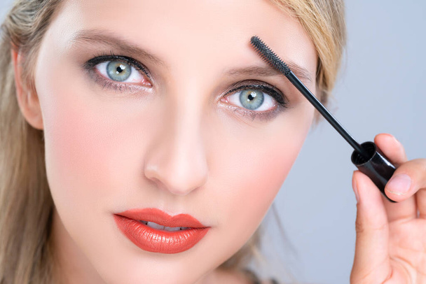 Closeup woman with blond hair putting alluring black mascara with brush in hand on long thick eyelash. Perfect fashionable cosmetic clean facial skin with beautiful eye young woman in high resolution. - Foto, immagini