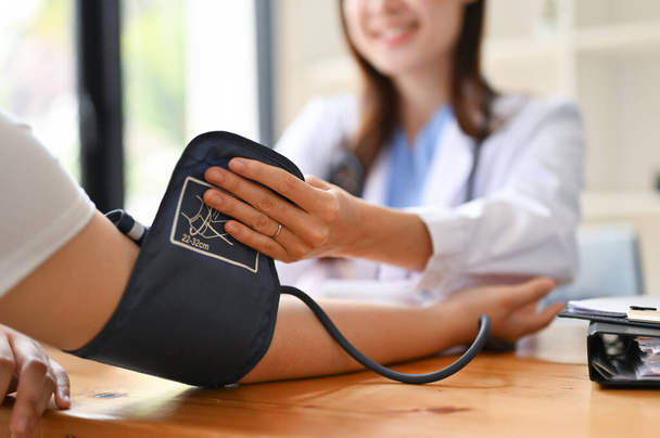 Imagen de cerca de una doctora asiática revisando el pulso, la frecuencia cardíaca y la presión arterial de una paciente con un monitor en la sala de examen. Concepto médico y sanitario - Foto, imagen