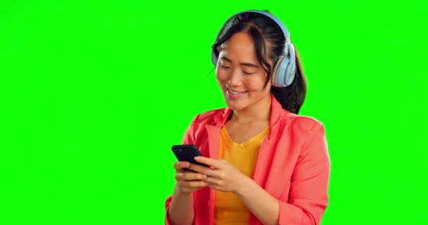 Yeşil ekran, telefon ve kulaklık stüdyo arka planında izole edilmiş bir kadın kahkahalar atıyor, mobil uygulamadan müzik dinliyor. Komik bir model için cep telefonunda, ses teknisyeninde veya video yayınında yazan Asyalı kişi. - Video, Çekim