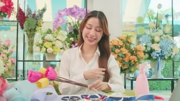 One Young beautiful Asian female florist entrepreneur arranging a bunch of blossoms, decorating with lovely ribbons, happy work in colorful flower shop store with blooms, and small business owner. - Filmmaterial, Video