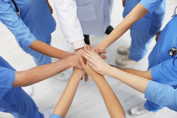 Doctor and interns stacking hands together indoors, closeup - 写真・画像