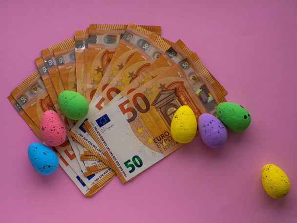 Velikonoční koncept s eurobankovkami a barevnými vejci na růžovém pozadí. Velikonoce a úspory, koncept utrácení peněz. Drahá oslava a nakupování velikonočních svátků. Šetřím peníze na dárky - Fotografie, Obrázek