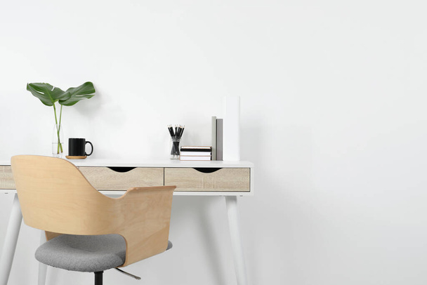 Comfortable workplace with white desk near wall. Space for text - Фото, изображение