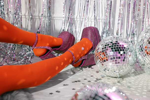 Woman in orange tights and pink high heeled shoes among disco balls indoors, closeup - Zdjęcie, obraz