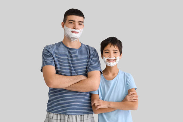 Vader en zijn zoontje met scheerschuim op gezicht tegen lichte achtergrond - Foto, afbeelding