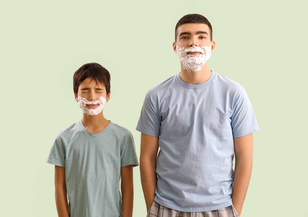 Человек и его маленький сын с пеной для бритья на лицах на светлом фоне - Фото, изображение