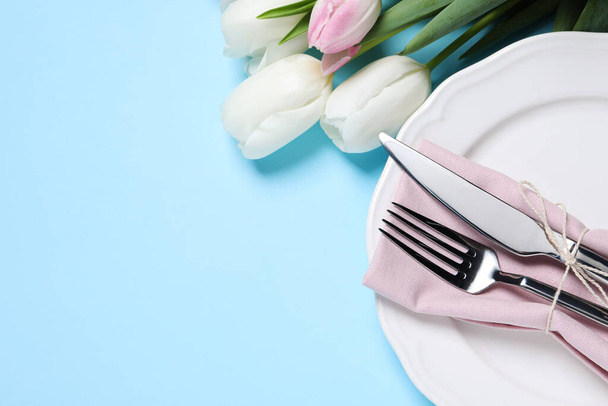 Stylish table setting with cutlery and tulips on light blue background, flat lay. Space for text - Fotografie, Obrázek