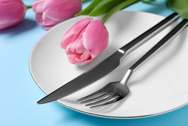 Stylové nastavení stolu s příbory a tulipány na světle modrém pozadí, detailní záběr - Fotografie, Obrázek