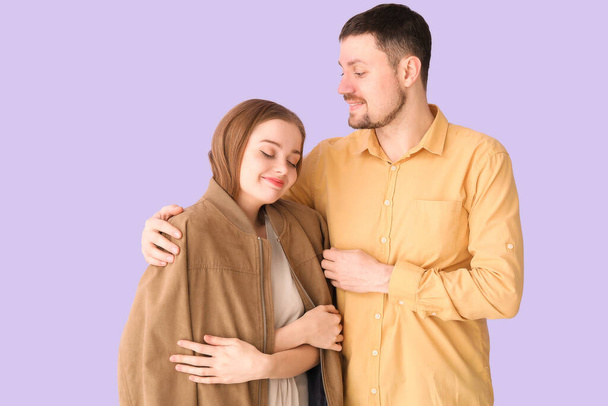 Νεαρός άντρας αγκαλιάζει τη γυναίκα του με το σακάκι του σε λιλά φόντο - Φωτογραφία, εικόνα