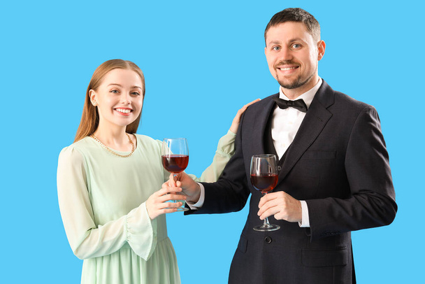 Ο νεαρός κουστουμάτος δίνει στη γυναίκα του ένα ποτήρι κρασί σε μπλε φόντο. - Φωτογραφία, εικόνα
