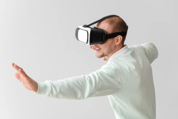 Young man using VR glasses on light background - Foto, afbeelding