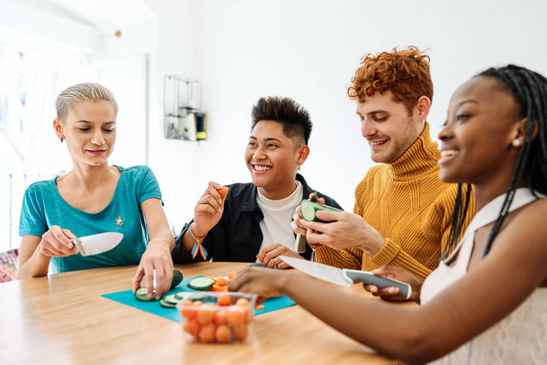 Groupe multiethnique d'amis préparant des aliments sains assis sur une table à la maison - Photo, image