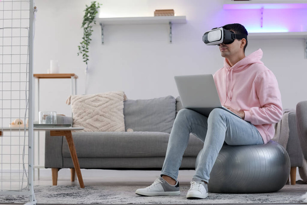 Νεαρός άνδρας που χρησιμοποιεί γυαλιά VR και φορητό υπολογιστή στο σπίτι - Φωτογραφία, εικόνα