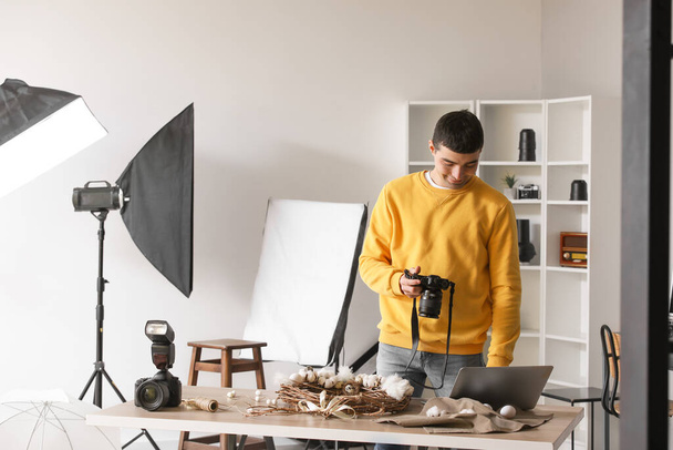 Jonge mannelijke fotograaf met professionele camera met laptop in de studio - Foto, afbeelding