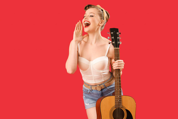 Young pin-up woman with guitar on red background - Fotó, kép