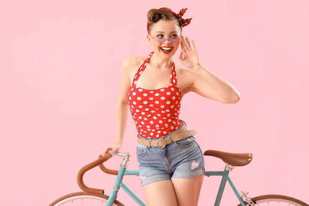 Young pin-up woman with bicycle on pink background - Foto, Imagen
