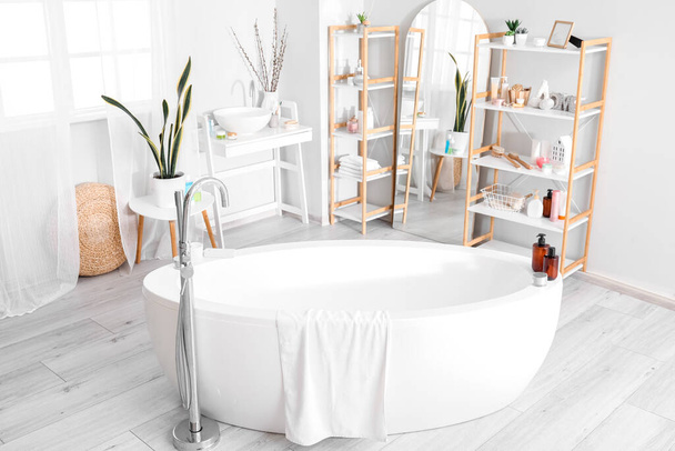Інтер'єр ванної кімнати з ванною, дзеркалом і стелажами
 - Фото, зображення