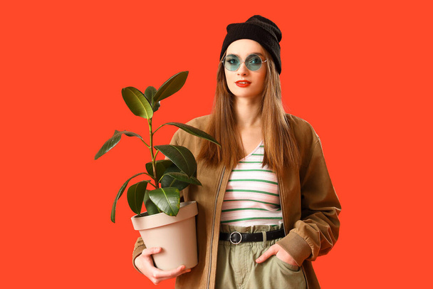 赤い背景に観葉植物を持つスタイリッシュな若い女性 - 写真・画像